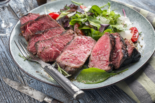 a sliced delmonico steak on a plate surrounded by greens