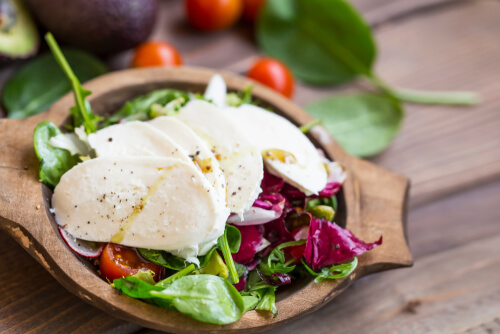 Four large slices of mozzarella cheese lay over top a salad