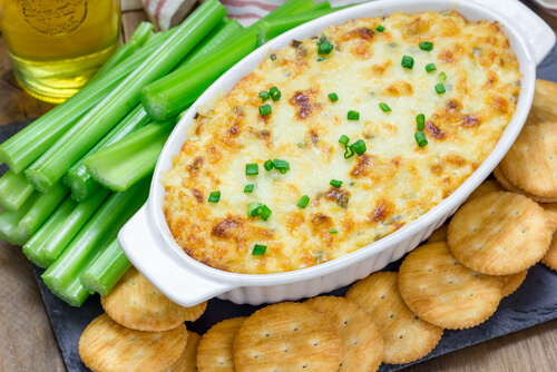 a white dish of canned crab dip with green onions sprinkled on top