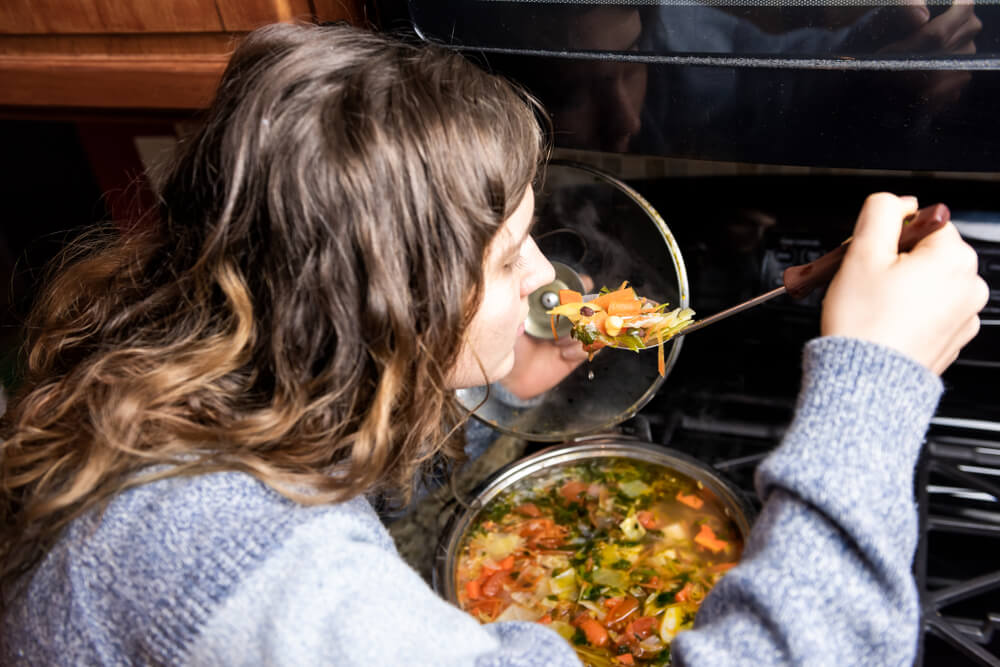 A woman tastes a spoonful of soup from the stove