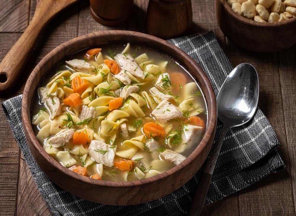 A bowl of chicken noodle soup on a place mat